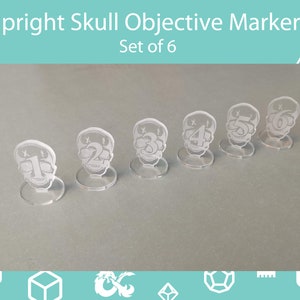 Op de afbeelding: Set van zes heldere acryl schedel objectieve markers, genummerd van 1 tot en met 6. Elke marker heeft een schedelontwerp en een cirkelvormige basis. De tekst "Upright Skull Objective Markers Set of 6" staat bovenaan de afbeelding.