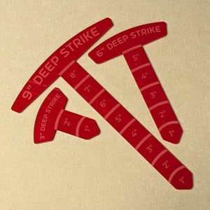 May include: Three red Deep Strike measuring tools. The largest reads 9" and the smallest reads 3". Each tool has inch markings. The text "DEEP STRIKE" is printed on each tool.