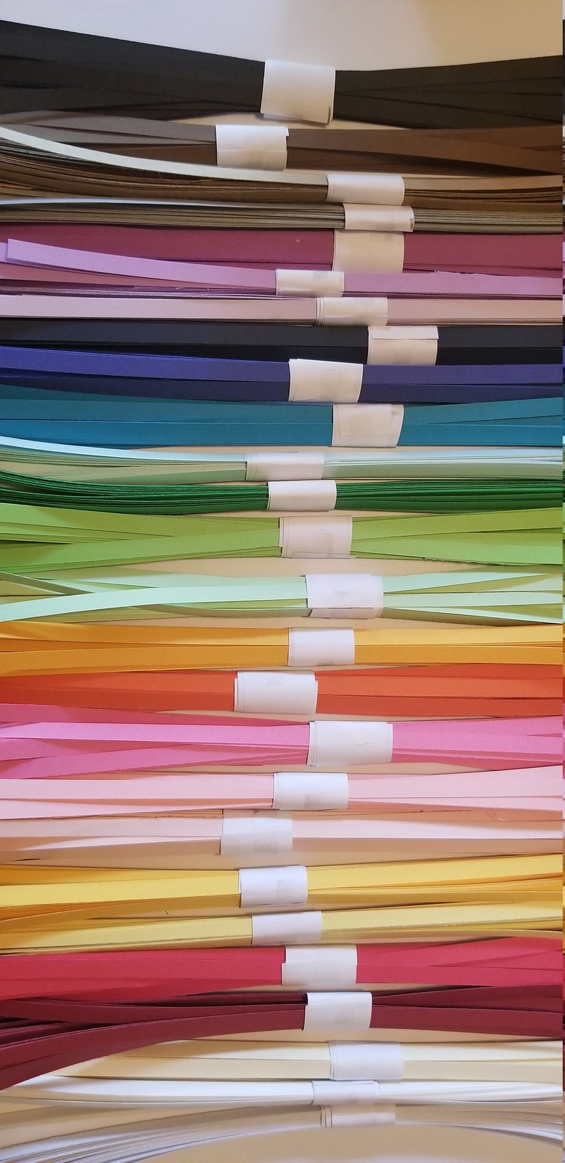 Puede incluir: Una pila de tiras de papel de colores, cada paquete est&aacute; atado con una etiqueta blanca. Los colores incluyen negro, marr&oacute;n, morado, rosa, azul, verde, amarillo, naranja, rojo y blanco.