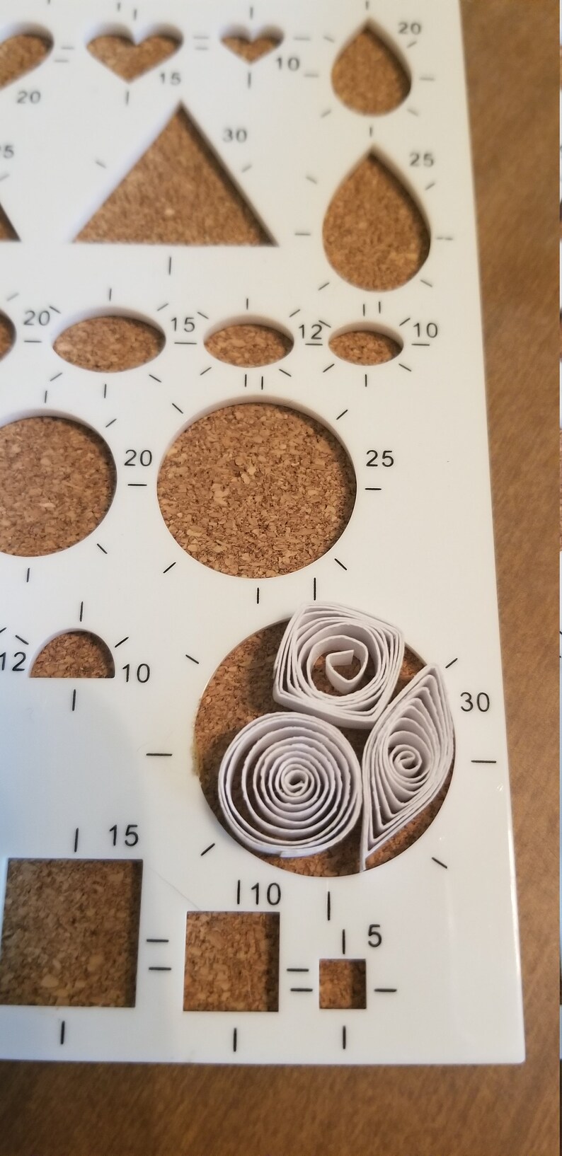 Puede incluir: Plantilla de pl&aacute;stico blanco con varias formas y tama&ntilde;os para manualidades. La plantilla tiene n&uacute;meros impresos en ella, incluyendo 5, 10, 12, 15, 20, 25 y 30. Hay tres formas de quilling de papel blanco en el centro de la plantilla.