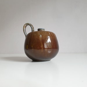 May include: A brown ceramic sugar bowl with a light blue glaze and a curved handle.
