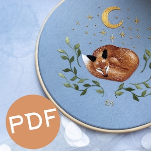 May include: Embroidered hoop art featuring a sleeping fox with a crescent moon and stars on a light blue background.