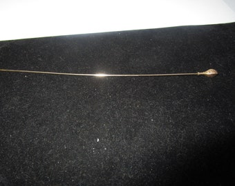 May include: A gold-toned hat pin with a decorative, openwork design on the top.