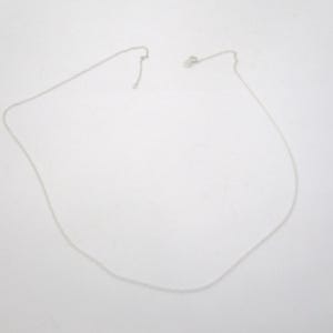 May include: A delicate silver necklace with a simple chain and clasp, lying on a white surface. The necklace is unadorned, showcasing a minimalist design. The chain appears to be approximately 18 inches long.