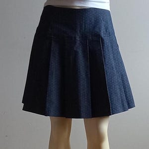 May include: A black pleated skirt with a white polka dot pattern. The skirt is knee-length and has a fitted waistband.