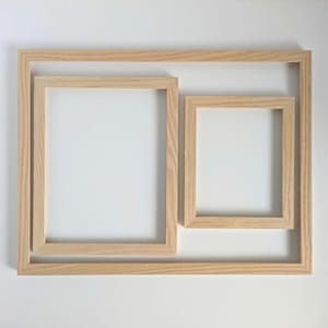 May include: A set of three rectangular light-coloured wooden frames arranged in a nested composition. The frames feature a visible natural wood grain texture and simple, clean edges, creating a layered appearance with varying sizes.