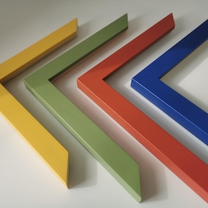 May include: A collection of colorful picture frame corners in yellow, green, red-orange, and blue. The frames are angled, showing their beveled edges and glossy finish. The arrangement suggests a display of various frame options.