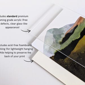May include: Close-up of a framed art print featuring a watercolor landscape with green, brown, and gray hues. The print is protected by clear acrylic and acid-free foam board backing for lightweight hanging.