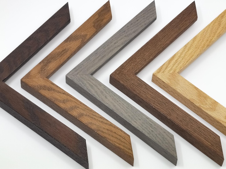 Solid oak picture frame corner samples sit on a plain white background. They are 1 inch wide by 3/4 inches high with a square profile. There are different stain colors: a dark "cocoa" brown which looks similar to espresso, "chestnut" which is a light brown with slight orange undertones, "light grey", "walnut" which is the second darkest brown with more of a red undertone, and "natural" which only has a clear varnish.