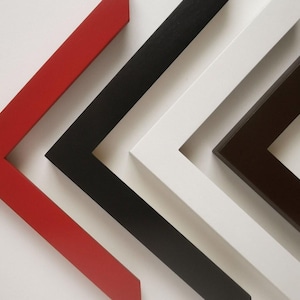 May include: A close-up shot of four picture frame corners in red, black, white, and brown. The frames are angled, displaying the different colours and the clean lines of the design. The background is plain white.