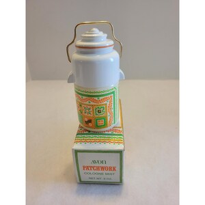 May include: A white plastic cologne bottle with a gold-tone wire handle, featuring a green and orange patchwork pattern. The bottle sits on a matching rectangular box labeled Avon Patchwork Cologne Mist Net Wt 3 oz with a decorative border.