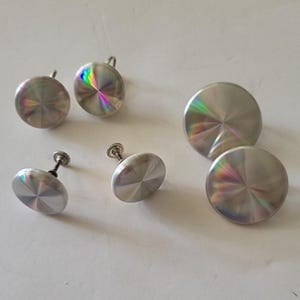 May include: A collection of silver-toned cabinet knobs and drawer pulls. The hardware features a circular design with a radial pattern and iridescent highlights. Some pieces have a screw-in design, while others have a loop for hanging.