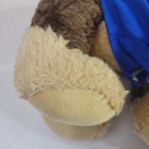 May include: Brown and tan plush dog toy wearing a blue shirt. The dog is lying down, and its paws are visible. The fur is soft and fluffy. The shirt has some text on it that is not clearly visible. The toy is suitable for children and is made of high-quality materials.