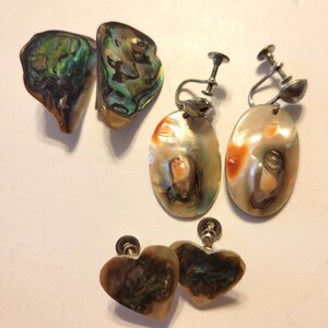 May include: A collection of vintage earrings featuring iridescent abalone shells. The earrings include clip-ons and post-style designs in various shapes, including oval and heart. The shells display a range of colors, including green, blue, and orange.