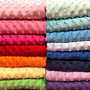May include: Stacks of colorful, textured fabric in various shades. The left side features pink, red, orange, yellow, and green. The right side displays teal, blue, white, navy, and purple. The fabric has a soft, dotted surface.