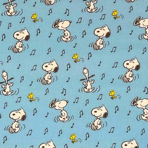 May include: Light blue fabric featuring a repeating pattern of Snoopy dancing with musical notes and Woodstock. The cartoon characters are in black and white, with yellow accents. The musical notes are black.