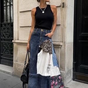 Puede incluir: Una camiseta de tirantes negra sin mangas combinada con una falda larga de mezclilla de retazos. La falda presenta paneles de mezclilla azul oscuro, una sección blanca desgastada, un inserto de tela con estampado de leopardo y un panel floral.