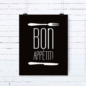 May include: A black poster with white text and cutlery illustrations. The words "BON APPÉTIT!" are centered, with a fork above and a knife below. The poster is clipped to a white brick wall.