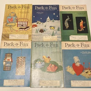 May include: Six vintage "Pack-O-Fun" magazines are displayed. The covers showcase craft projects such as a butterfly purse, winter scenes, and decorative lanterns. The magazines are in various colors, including yellow, blue, and green.