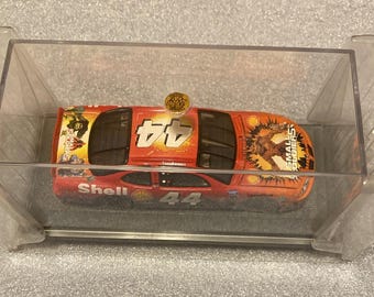 May include: A red and orange toy race car with the number 44 on the sides and top, displayed in a clear plastic case. The car has Shell branding and "Small Soldiers" graphics.