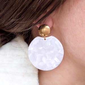 Peut inclure: Boucles d'oreilles rondes blanches avec une surface texturée et des accents dorés.