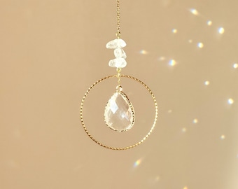 May include: A gold chain with a clear crystal teardrop pendant hanging from a gold circle. The crystal is faceted and reflects light.