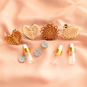 May include: Four woven wicker car air freshener clips in the shapes of a heart, sun, and two circles. Three clear glass bottles with gold caps and gray felt pads.