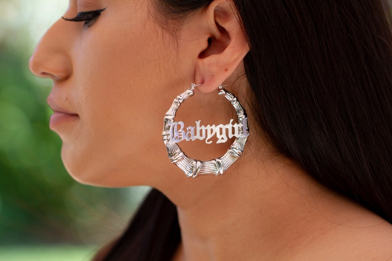 K&ouml;nnte beinhalten: Silberne Creolen mit Bambus-Design. Die Ohrringe zeigen das Wort "Babygirl" in einer gotischen Schrift.