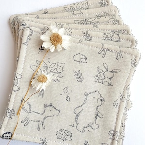 Könnte beinhalten: Ein Stapel von 10 beigen Baumwoll-Schminkpads mit einem Waldtier-Druckmuster. Der Druck zeigt einen Fuchs, einen Bären, ein Kaninchen und einen Igel. Die Pads haben einen ausgefransten Rand.