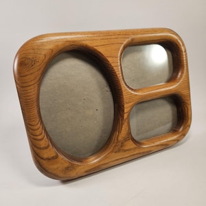 May include: A multi-opening picture frame crafted from light brown wood with a prominent grain pattern. The frame features one large oval-shaped opening on the left side and two smaller rectangular openings with rounded corners on the right side.