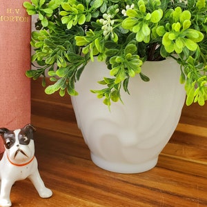 May include: Two vintage hardcover books, "The Children's Classics" and "The Call of England" by H.V. Morton, are stacked on a wooden shelf. A white ceramic dog figurine sits in front of the books. A white ceramic planter with a green leafy plant is on the shelf.