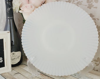 May include: A white, fluted, ceramic plate with a blue rim sits on a clear stand. The plate is on a wooden surface with a black letter board that says "Hello Gorgeous" and a bottle of champagne.