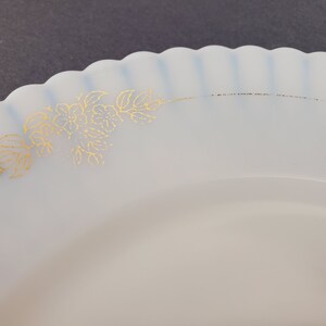 May include: A white ceramic plate with a scalloped edge and a gold floral design. The plate is perfect for serving desserts or appetizers.