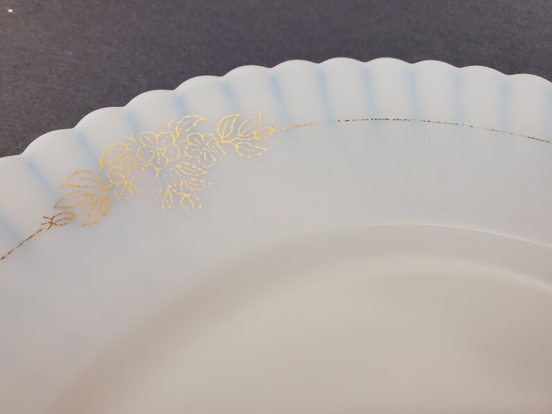 May include: A white ceramic plate with a scalloped edge and a gold floral design. The plate is perfect for serving desserts or appetizers.