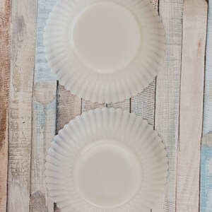 May include: Two white ceramic plates with scalloped edges. The plates are on a wooden background.