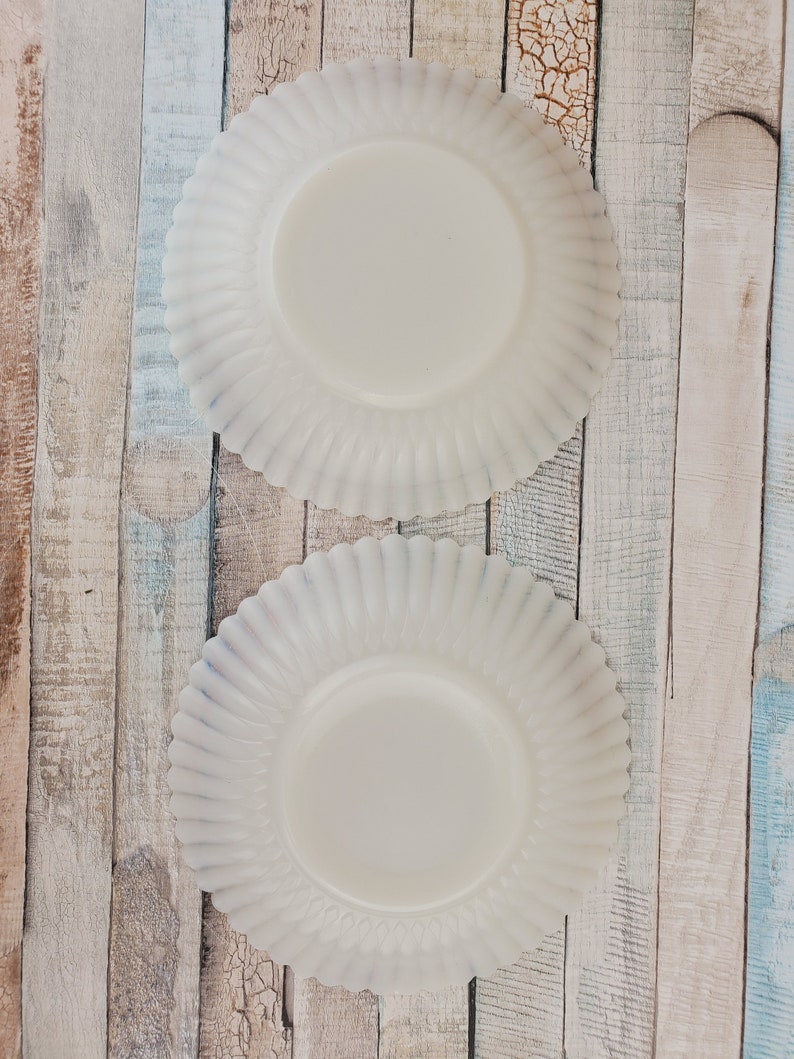 May include: Two white ceramic plates with scalloped edges. The plates are on a wooden background.