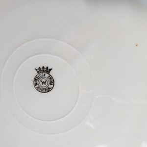 K&ouml;nnte beinhalten: Nahaufnahme einer wei&szlig;en Keramikplatte mit einem schwarz-wei&szlig;en Logo, das "Wheel ock China Austria" mit einer Krone &uuml;ber dem "W" lautet.