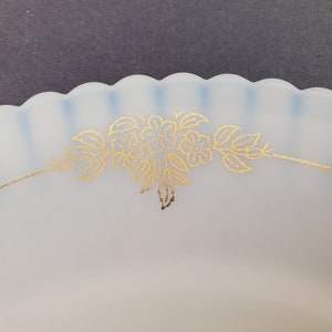 May include: A white frosted glass plate with a scalloped edge and a gold floral design. The plate has a blue tint around the edge.