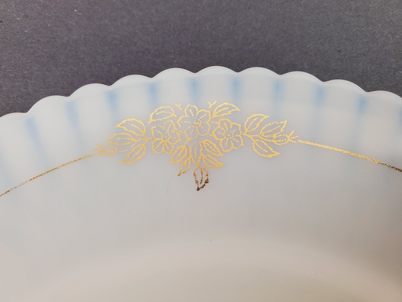May include: A white frosted glass plate with a scalloped edge and a gold floral design. The plate has a blue tint around the edge.