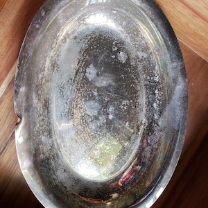May include: A silver oval serving dish with a slightly tarnished finish. The dish has a raised rim and a smooth, reflective surface.
