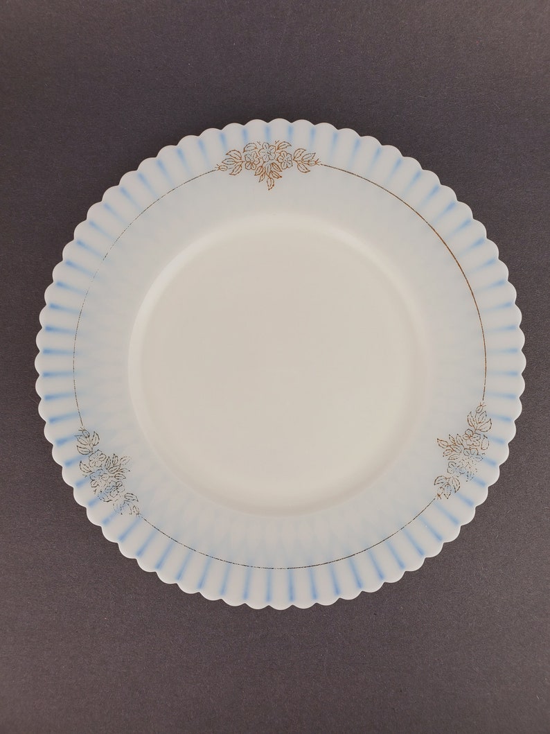 May include: A white ceramic plate with a blue and gold floral design. The plate has a scalloped edge.
