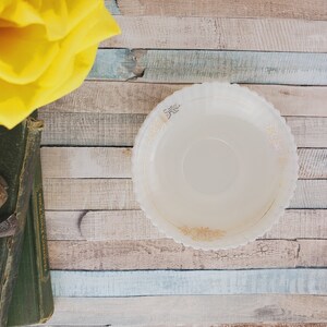 May include: A white, scalloped-edge bowl with a gold floral design sits on a wooden surface. The bowl is empty.