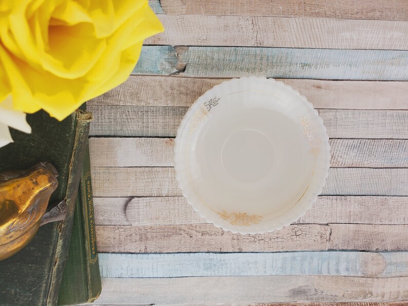 May include: A white, scalloped-edge bowl with a gold floral design sits on a wooden surface. The bowl is empty.