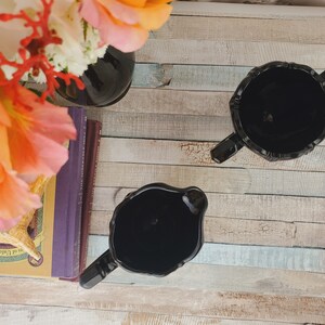 K&ouml;nnte beinhalten: Zwei schwarze Glask&auml;nnchen mit dekorativem Design auf einer Holzoberfl&auml;che.