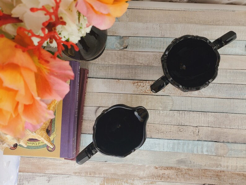 K&ouml;nnte beinhalten: Zwei schwarze Glask&auml;nnchen mit dekorativem Design auf einer Holzoberfl&auml;che.