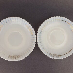 May include: Two white, scalloped-edge saucers with a blue and gold floral design. The saucers are made of opaque glass and have a raised center.
