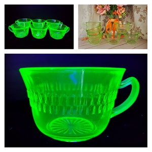 May include: Set of six green uranium glass teacups. The cups are clear and have a textured design. The cups are arranged in a row on a black surface.