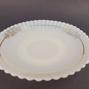 May include: A white, scalloped-edge saucer with a blue and gold floral design. The saucer has a raised center and a smooth, glossy finish.