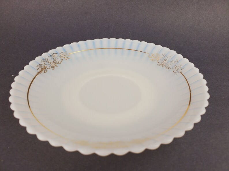 May include: A white, scalloped-edge saucer with a blue and gold floral design. The saucer has a raised center and a smooth, glossy finish.