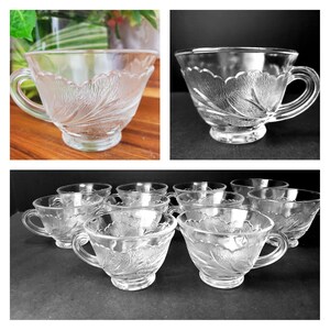 Könnte beinhalten: Klare Teetassen aus Glas mit einem floralen Blattdesign. Jede Tasse hat einen Henkel und steht auf einem kleinen Sockel. Das Bild zeigt einzelne Tassen und ein Set mit mehreren Tassen.